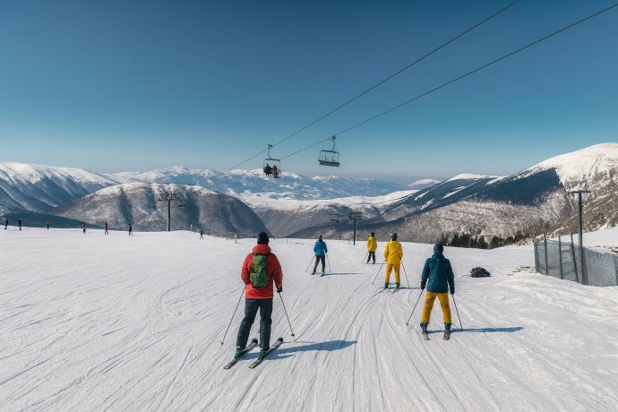 Sciatori sulle piste di Frontignano 360 con seggiovia Saliere e Monte Bove sullo sfondo, cielo blu.