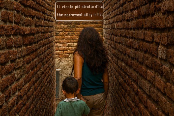 Donna e bambino nel vicolo più stretto d’Italia a Ripatransone, tra mura di mattoni.