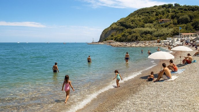 Baia Vallugola a Gabicce Mare: spiaggia di ciottoli, ombrelloni bianchi e acqua turchese nel San Bar