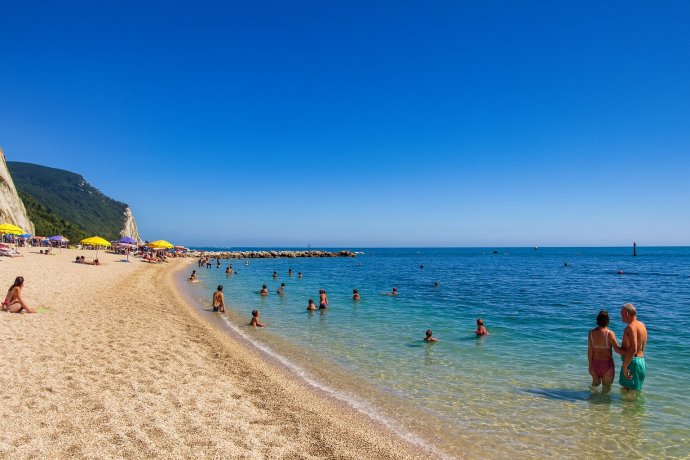 Spiaggiola di Numana: spiaggia di ciottoli, mare turchese, ombrelloni, Conero sullo sfondo.