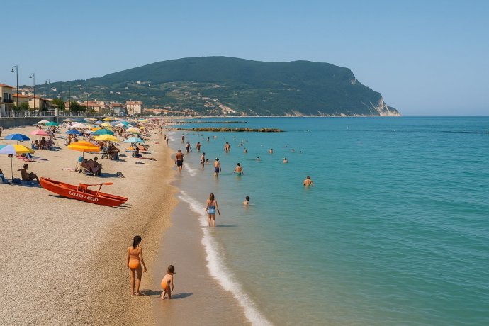 Porto Recanati: spiaggia di ghiaia con ombrelloni, bagnanti e Monte Conero sullo sfondo. 