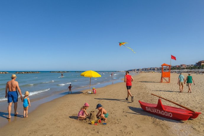 Porto San Giorgio, spiaggia sabbiosa con mare calmo, pattino salvataggio, bimbi e aquilone.