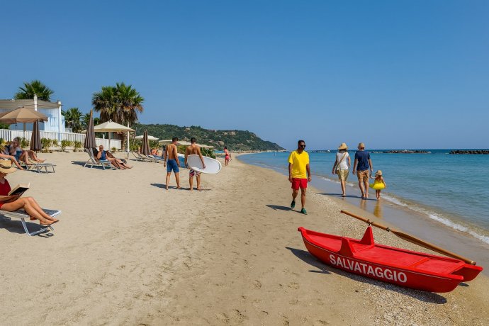 Spiaggia di Campofilone, mare calmo e pattino rosso salvataggio; famiglia e ragazzi con SUP.