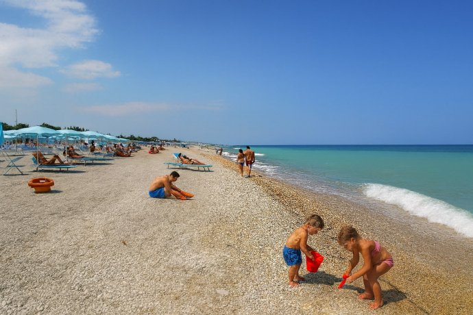 Spiaggia di Porto Sant’Elpidio con mare turchese, ombrelloni azzurri e bambini sulla riva.
