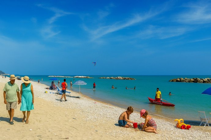 piaggia di Pedaso con mare turchese, frangiflutti, coppia a passeggio, bimbi e barca salvataggio.