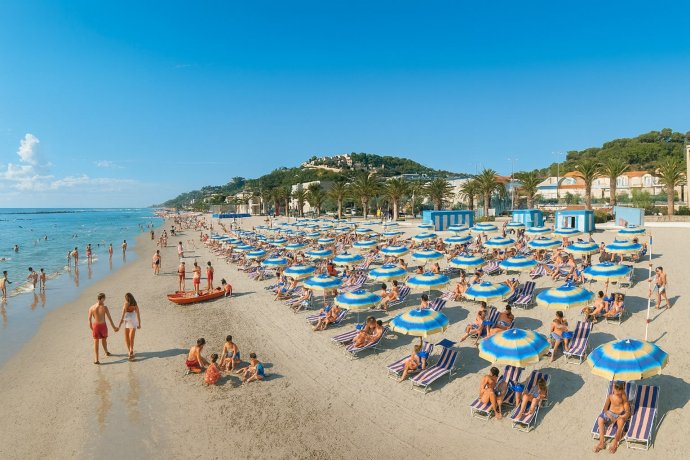 Cupra Marittima: spiaggia con ombrelloni giallo-blu, bagnanti e mare calmo sotto cielo terso.
