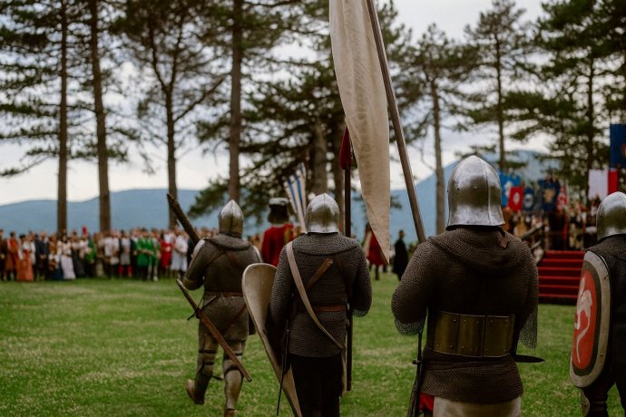 Corsa alla Spada e Palio di Camerino: cavalieri in armatura tra i pini, pubblico sullo sfondo. 