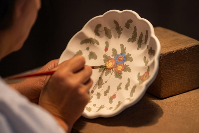 Mano di artigiana che dipinge a mano un piatto in ceramica decorata a motivi floreali.