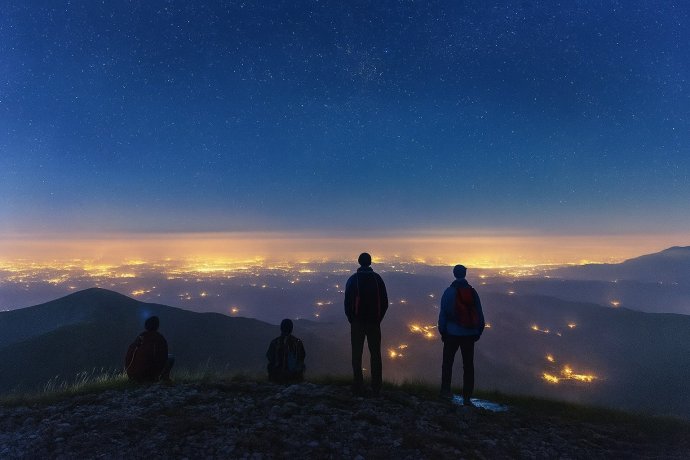 Escursionisti sui Monti Sibillini di notte osservano le luci della valle sotto un cielo stellato.