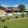 Edificio con giardino ben curato, siepi e fiori sotto un cielo blu.