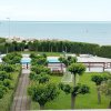 Vista su piscina, giardino con alberi e siepi, e mare sullo sfondo.