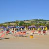 Lettini e ombrelloni colorati su una spiaggia sabbiosa, collina verde sullo sfondo.