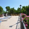 Una terrazza con sedie a sdraio a righe bianche e blu, circondata da fiori rosa e piante verdi.