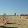 Spiaggia con sdraio rosso-arancio, ombrelloni variopinti e mare calmo.