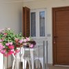 Un piccolo patio con fiori rosa, tavolo bianco con sedie, porta in legno e finestra.