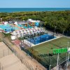 Vista aerea di un centro sportivo con piscine, campi sportivi e ombrelloni vicino al mare.