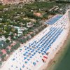 Spiaggia con ombrelloni blu e bianchi allineati, case e vegetazione sullo sfondo.