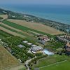 Vista aerea di un paesaggio rurale con campi verdi, edifici e il mare sullo sfondo.