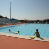 Piscina all'aperto con bambini che nuotano. Lettini e ombrelloni lungo i bordi.