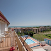 Vista di un balcone con piscina, edifici e mare sullo sfondo.