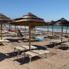 Lettini e ombrelloni vuoti su una spiaggia sabbiosa con onde in lontananza.