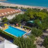 Vista aerea di una piscina vicino alla spiaggia, circondata da alberi e ombrelloni.
