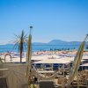 Spiaggia con ombrelloni bianchi, arancioni e blu. Palme e montagne all'orizzonte.
