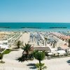 Spiaggia affollata con ombrelloni colorati, palme e mare blu sullo sfondo.