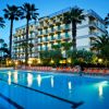 Hotel con piscina illuminata di sera, circondato da palme e lettini arancioni.