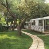 Case mobili bianche lungo un sentiero tra alberi e prato verde.