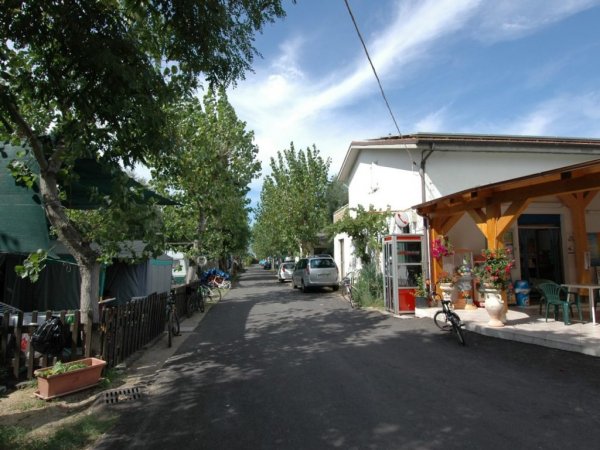 Strada con biciclette e automobili, fiancheggiata da edifici e aree per campeggio.