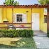 Una casa gialla con veranda in legno, sedie colorate e un barbecue nel giardino.