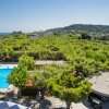 Vista di una piscina circondata da alberi con colline e mare sullo sfondo.