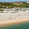Spiaggia con ombrelloni, mare calmo e persone su tavole da surf.