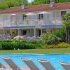 Villa con piscine, giardino fiorito, balconi e sdraio bianche in primo piano.
