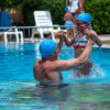 Uomo e bambino con cuffie da nuoto azzurre giocano in piscina.
