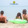 Tre persone in riva al mare, sedute sulla sabbia, con un gonfiabile verde.