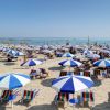 Spiaggia con ombrelloni blu e bianchi, lettini e bagnanti in mare.