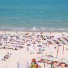 Vista aerea di una spiaggia affollata con ombrelloni colorati e mare in lontananza.