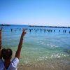 Persona sulla spiaggia con braccia alzate, gente in mare.