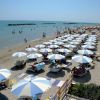 Spiaggia con ombrelloni bianchi e blu, e persone che si godono il sole e il mare.