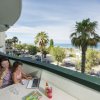 Due persone su un balcone con vista mare e palme.