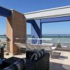 Terrazza moderna con sedie e divani, vista su mare e cielo blu.