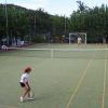 Ragazza con cappellino rosso gioca a tennis su un campo all'aperto.