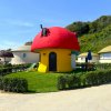 Casa a forma di fungo rosso con giardino e sedie a sdraio.