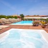 Piscina all'aperto con idromassaggio, lettini e ombrelloni, circondata da piante.
