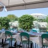 Tavola apparecchiata con sedie verdi sotto un gazebo con piante e piscina sullo sfondo.