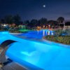 Piscina luminosa di notte con getti d'acqua e piante, sotto un cielo stellato.