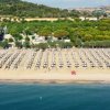 Spiaggia con file ordinate di ombrelloni e lettini, davanti a un paesaggio verde e collinare.