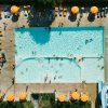 Piscina vista dall'alto con bagnanti e ombrelloni arancioni disposti attorno.